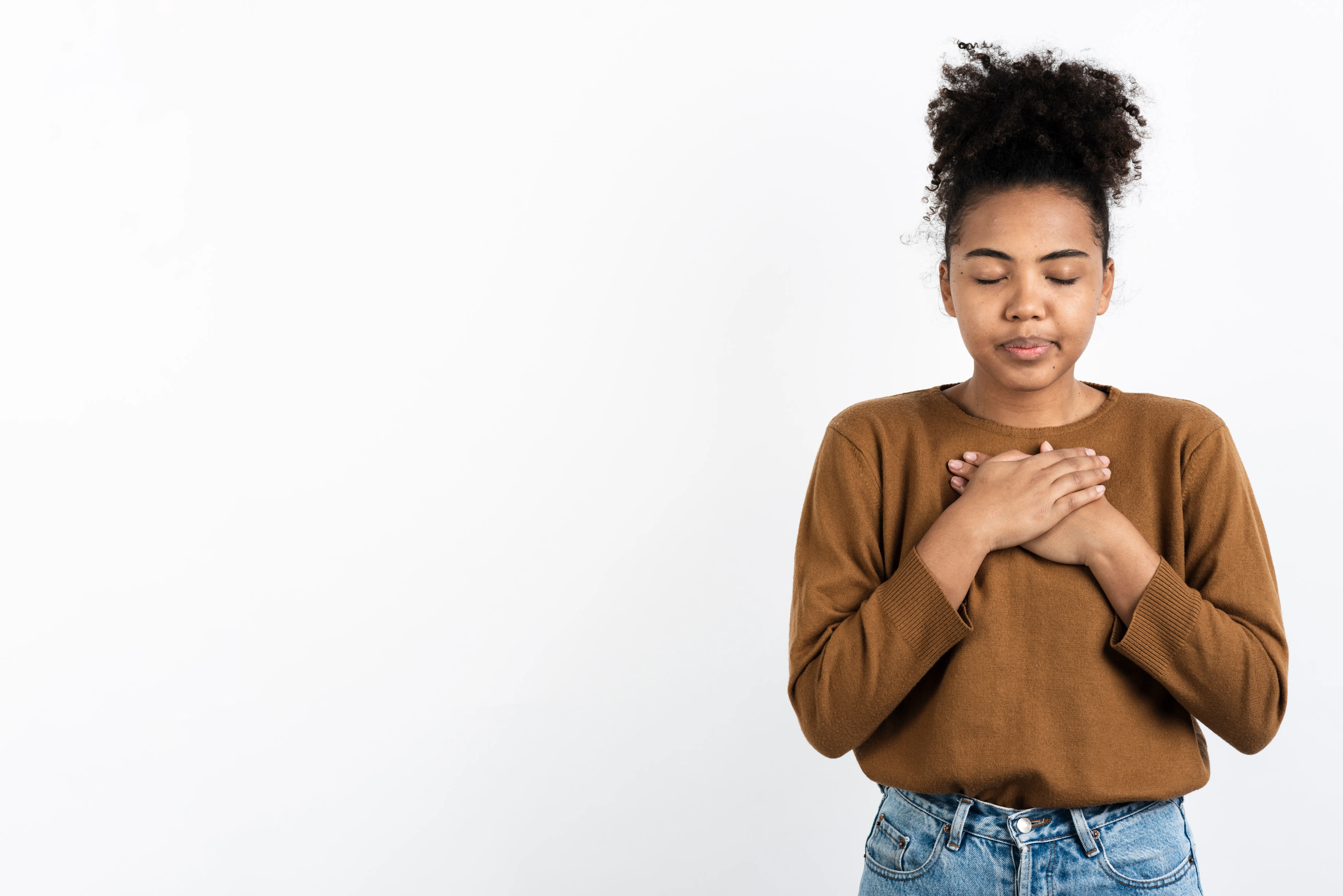 Une jeune femme les yeux fermés, les mains posées sur le cœur, en signe de recueillement.