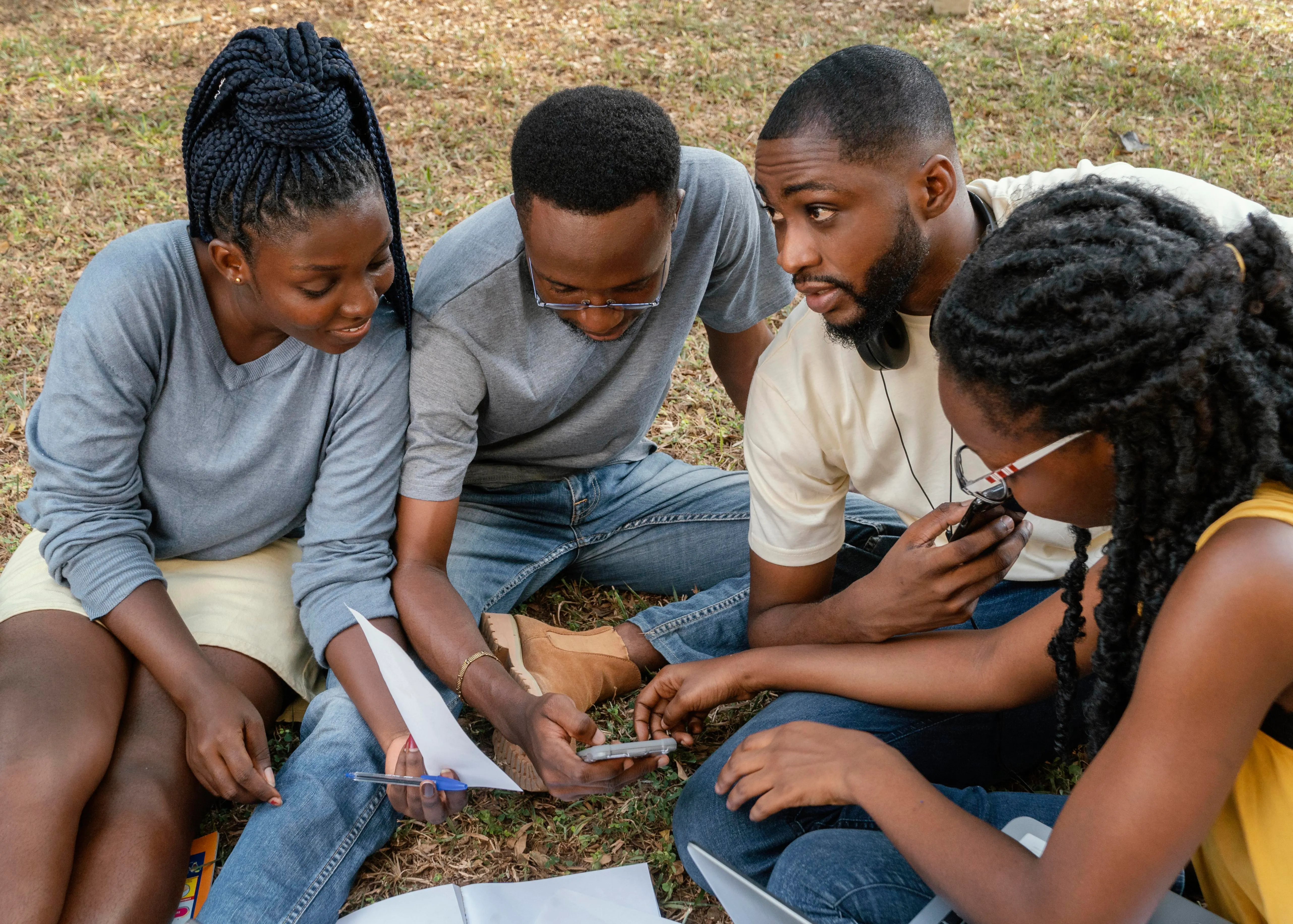 Un groupe de jeunes assis ensemble à l'extérieur, échangeant autour de documents.