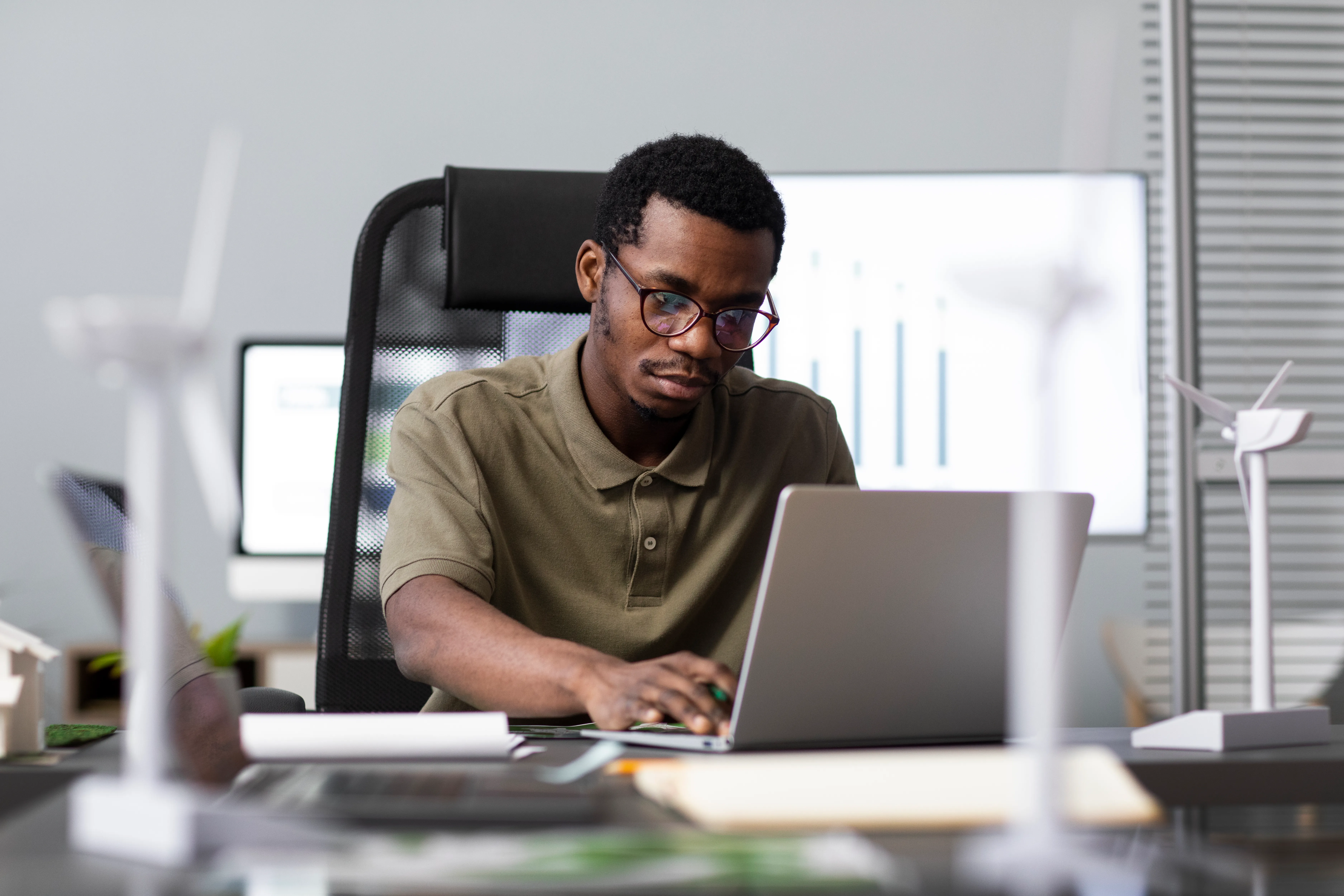 Un jeune homme concentré, travaillant sur un ordinateur portable dans un bureau moderne.