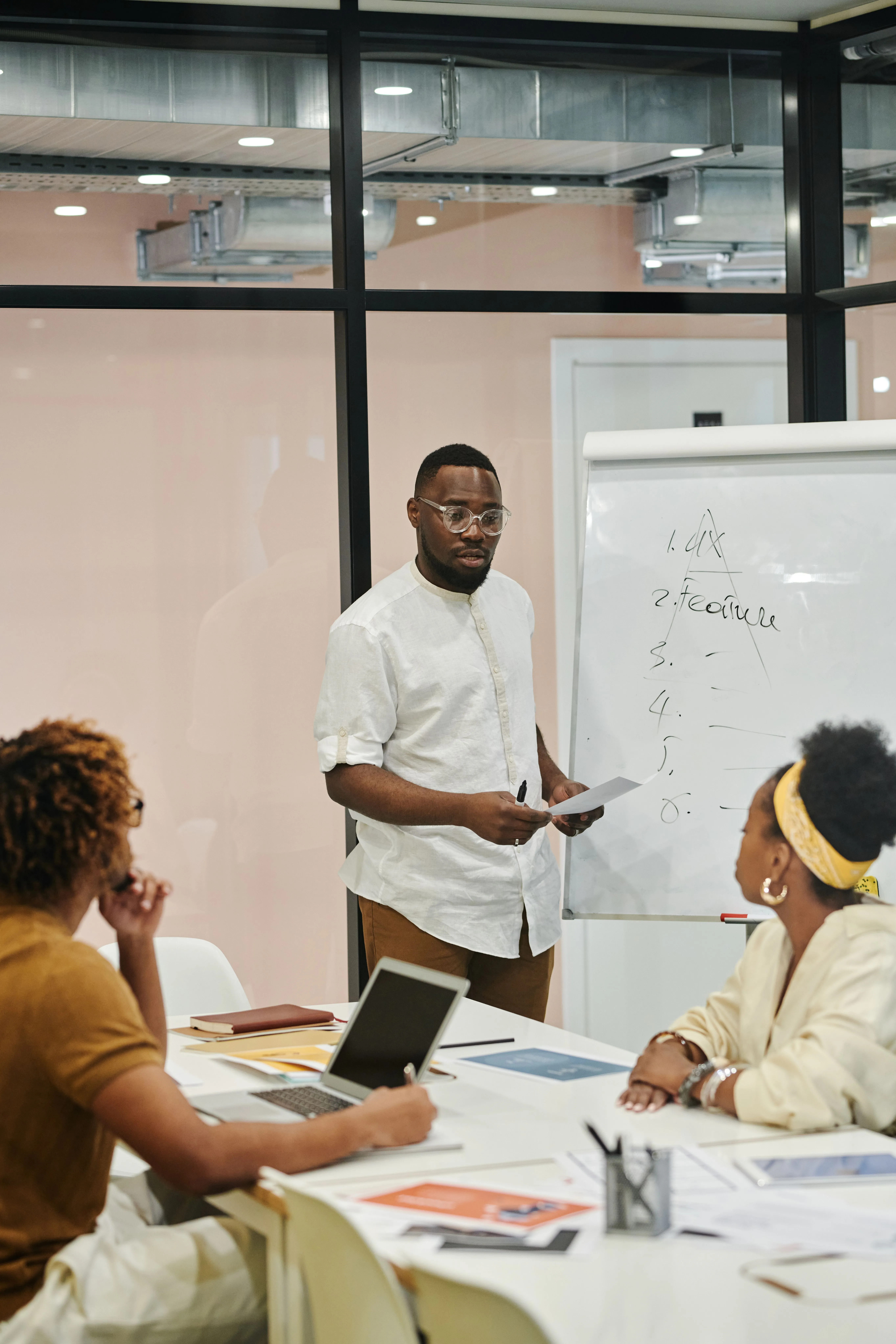 Un jeune homme présentant devant un tableau de conférence, entouré de collègues attentifs.