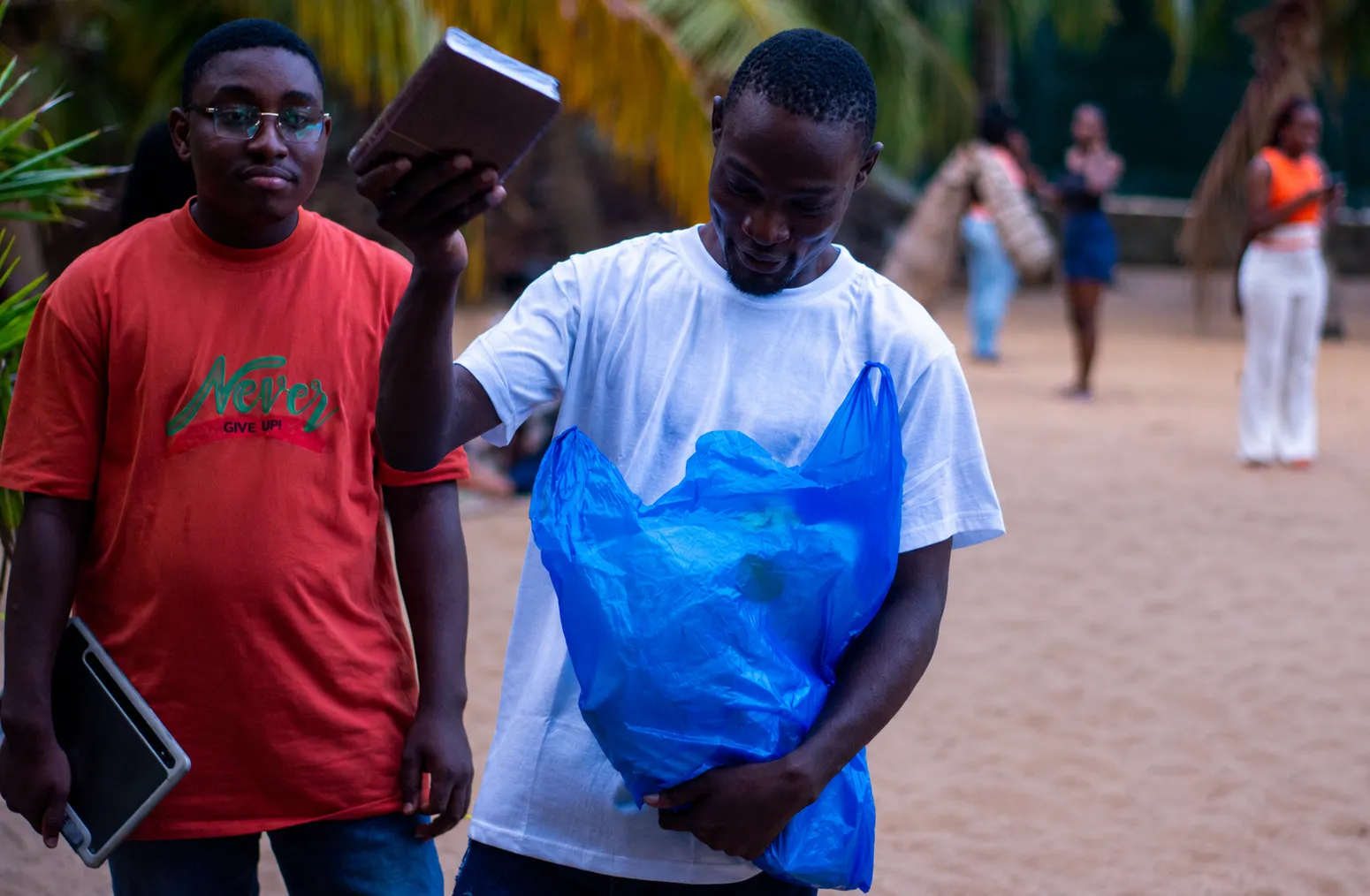 Un jeune homme tenant un sac de collecte pendant une action de nettoyage en extérieur, entouré d'autres participants.