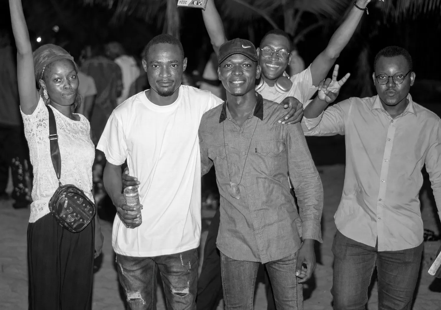 Un groupe de cinq jeunes souriants, bras levés, lors d'une rencontre en soirée.