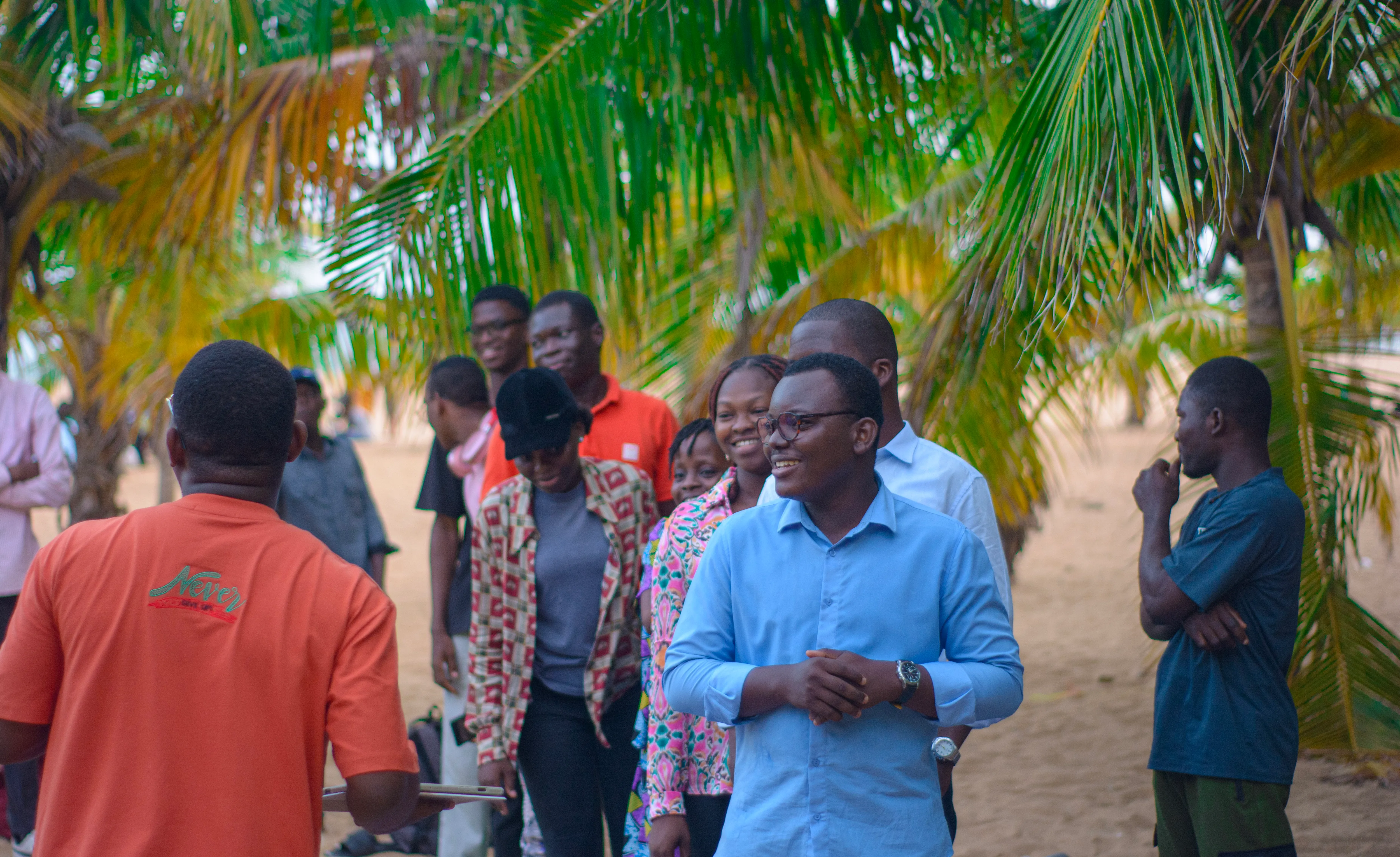 Un groupe de jeunes adultes souriants, marchant et échangeant ensemble sous des palmiers.
