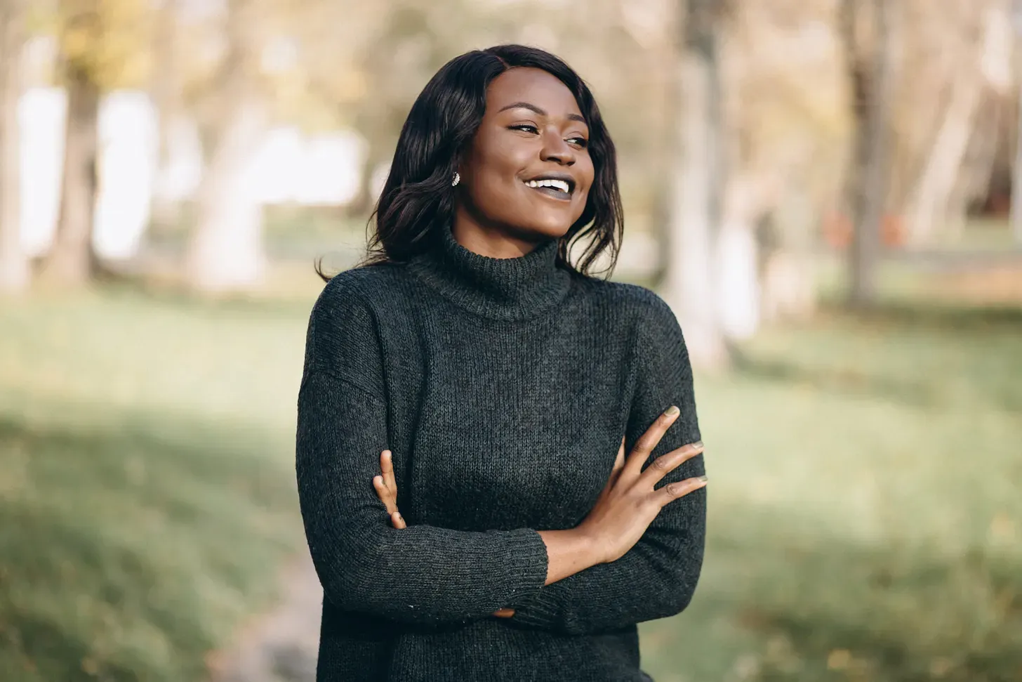 Une jeune femme souriante, bras croisés, dans un parc en automne.